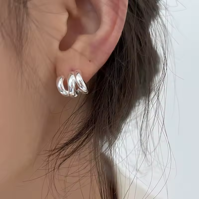 Gedrehte Silber-Creolen mit glänzender Oberfläche – getragen am Ohr, elegantes modernes Design.