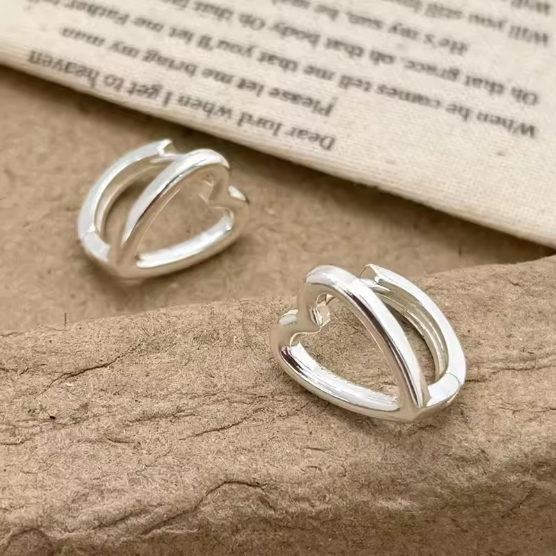 Herzförmige Creolen aus 925 Sterling Silber auf braunem Hintergrund, minimalistisches Schmuckdesign