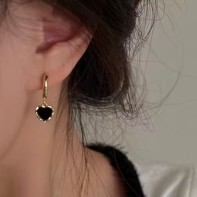 Elegante Huggies-Ohrringe aus 925 Sterling Silber mit schwarzem Herzanhänger, vergoldet mit 18K, auf weichem Stoffhintergrund.