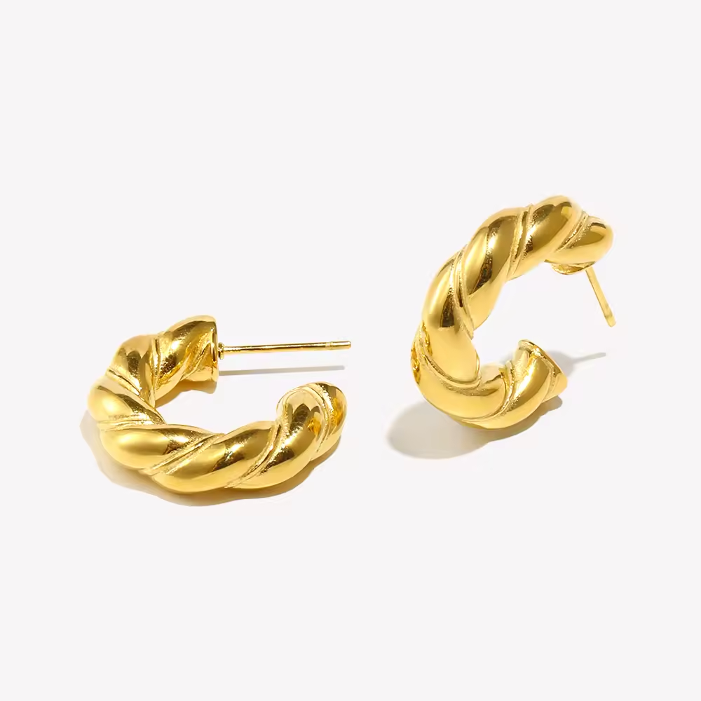 Gedrehte goldene Creolen mit glänzender Oberfläche auf hellem Hintergrund