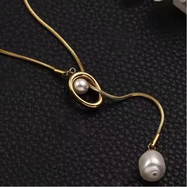 Goldene Y-Halskette mit seitlichem Ringanhänger und hängender Barockperle auf schwarzem Untergrund