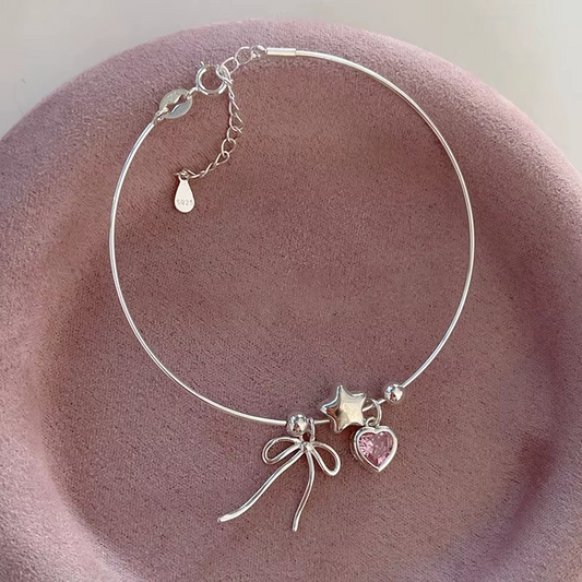 Silbernes Armband aus 925 Sterling Silber mit Herz-Zirkonia, Stern und Schleifenanhänger auf rosa Samt – verstellbares Schmuckstück für Frauen.