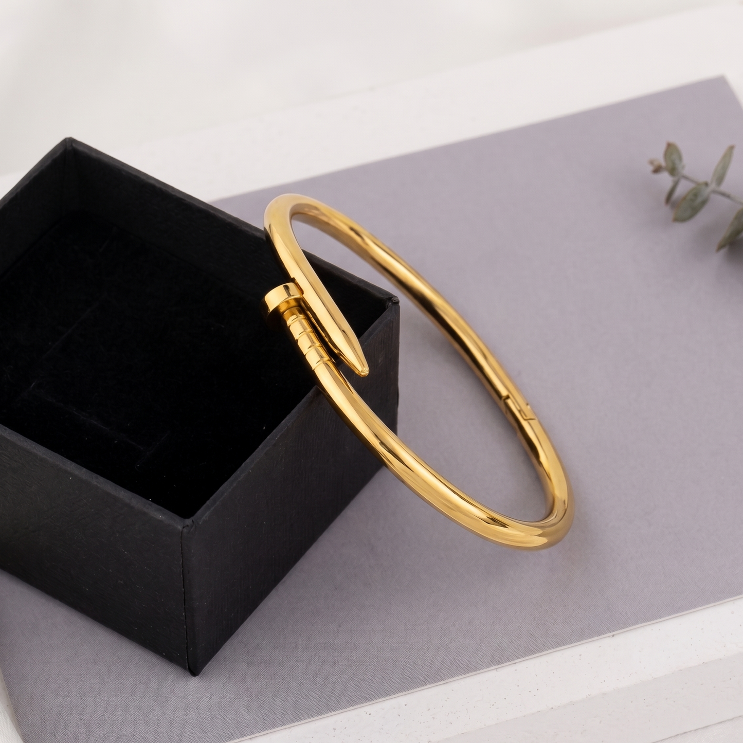Ein eleganter, goldener Nagel-Armreif der Marke BOGUE, getragen am Handgelenk einer Frau in Kombination mit feinen Perlenarmbändern auf beigem Leinenstoff.