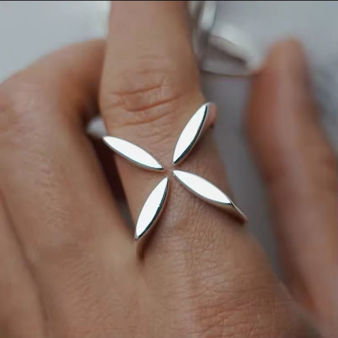Hand trägt einen silbernen Ring mit floralem Kreuz-Motiv in modernem Design.