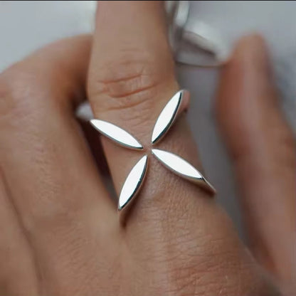 Hand trägt einen silbernen Ring mit floralem Kreuz-Motiv in modernem Design.
