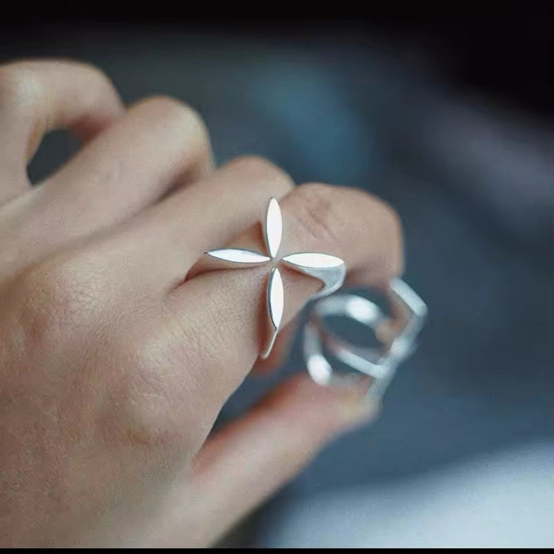 Hand trägt einen silbernen Ring mit floralem Kreuz-Motiv in modernem Design.