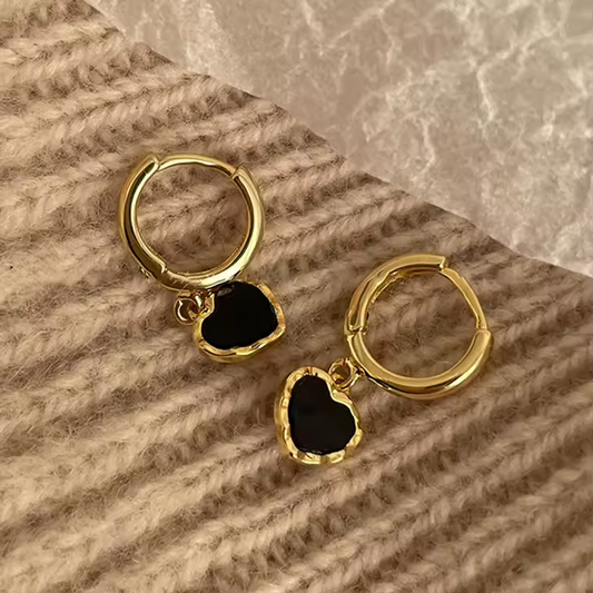 Elegante Huggies-Ohrringe aus 925 Sterling Silber mit schwarzem Herzanhänger, vergoldet mit 18K, auf weichem Stoffhintergrund.