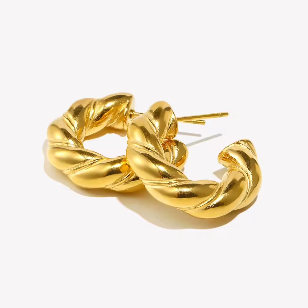 Gedrehte goldene Creolen mit glänzender Oberfläche auf hellem Hintergrund