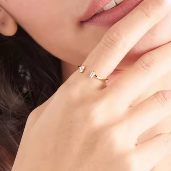 Vergoldeter, offener Ring mit zwei klaren länglichen Zirkonia-Steinen im modernen Design – Schmuckstück auf weißem Hintergrund

