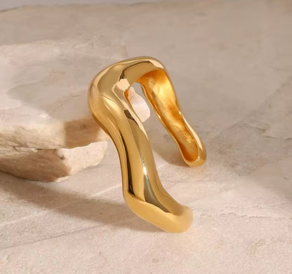 Goldener Edelstahl-Armreif mit fließender Wellenform auf weißem Hintergrund
