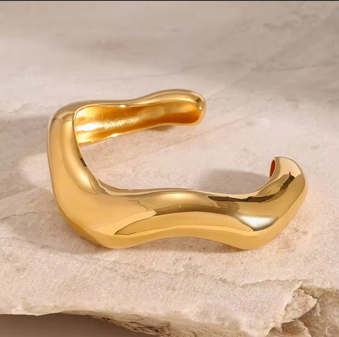 Goldener Edelstahl-Armreif mit fließender Wellenform auf weißem Hintergrund“
