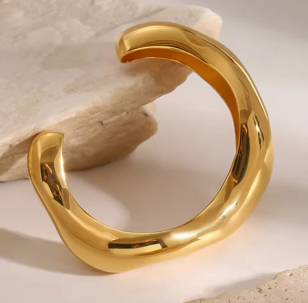 „Goldener Edelstahl-Armreif mit fließender Wellenform auf weißem Hintergrund
